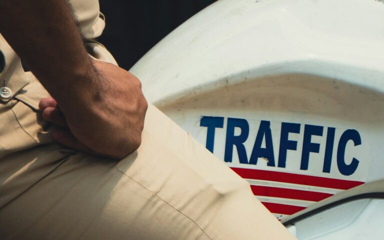 Driver reviewing an out-of-state traffic citation beside a vehicle with road signs visible in the background.